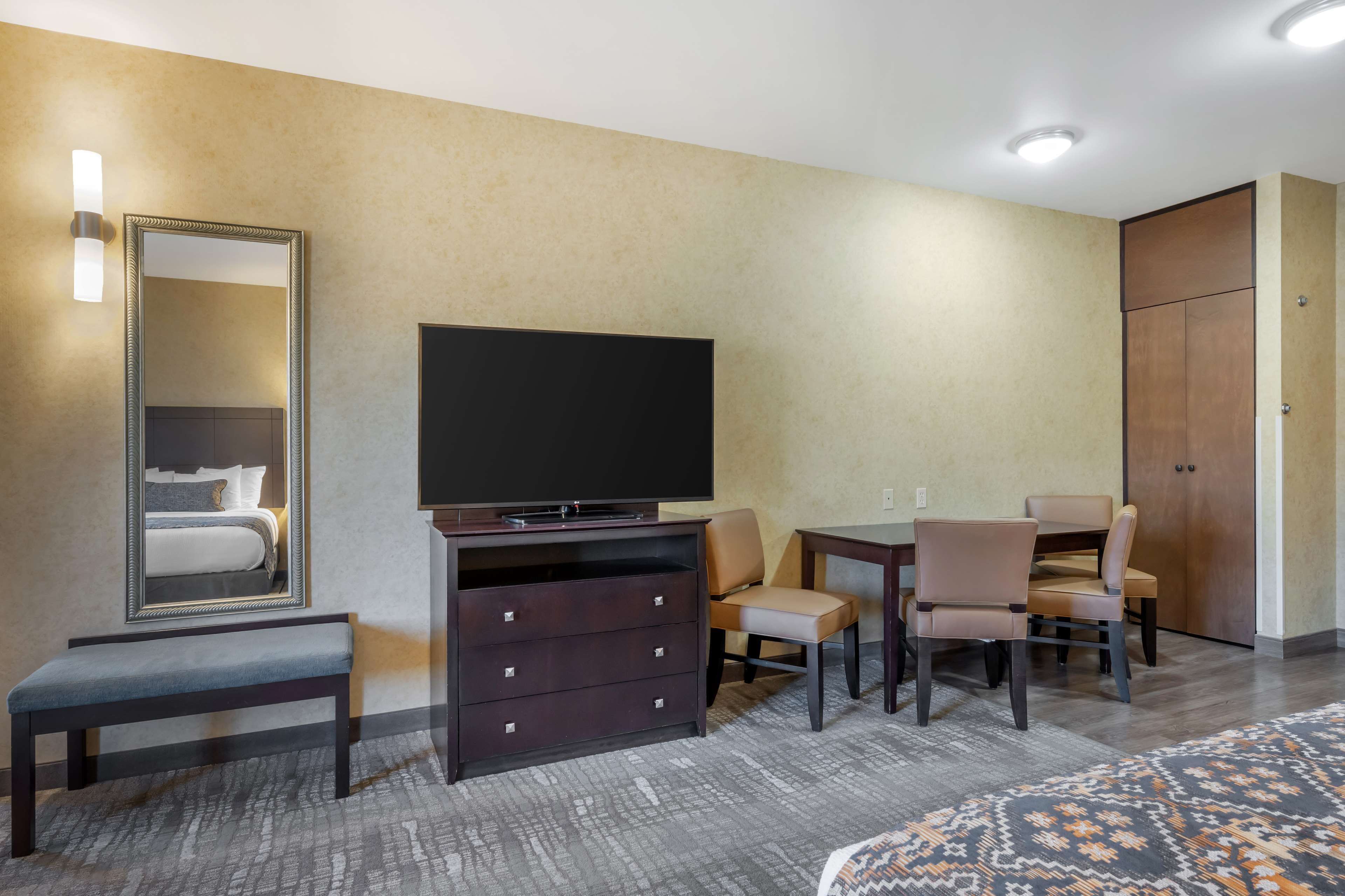 A hotel room with a bed, a TV, a dresser, a desk with chairs, and a wardrobe.