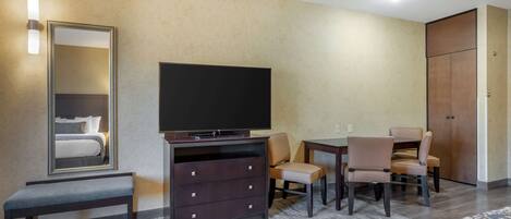 A hotel room with a bed, a TV, a dresser, a desk with chairs, and a wardrobe.