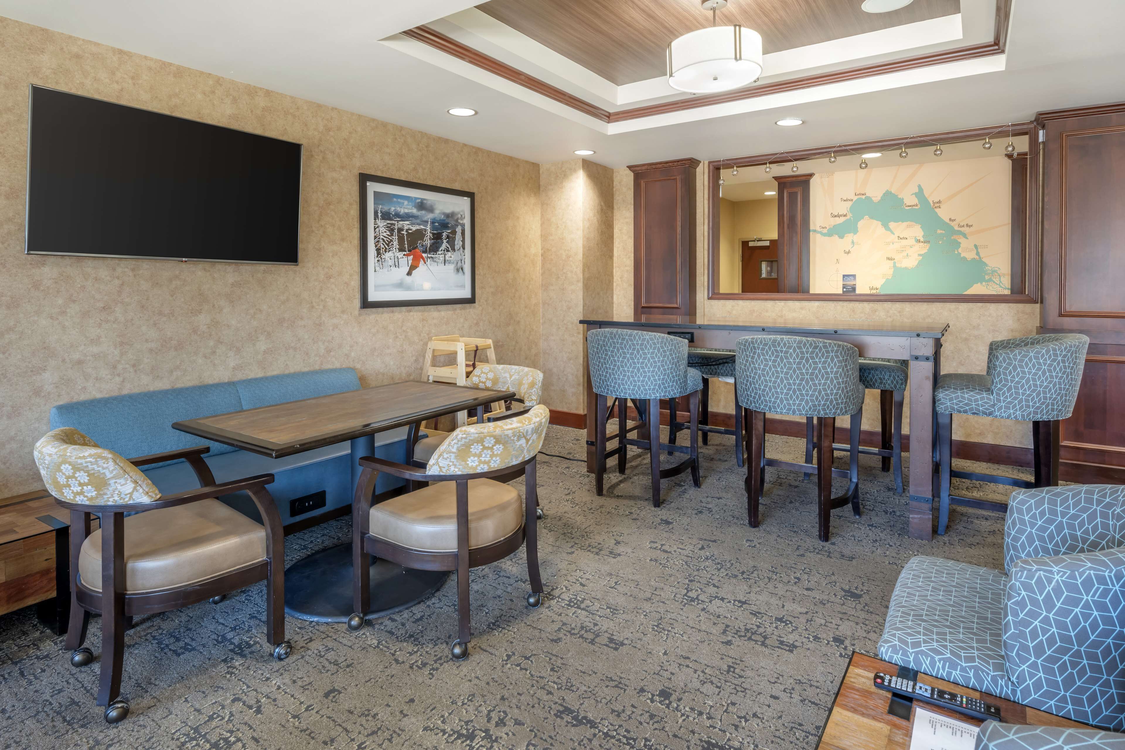 A hotel lobby with a large flat-screen TV, a map on the wall, a blue sofa, and a bar area with patterned stools.