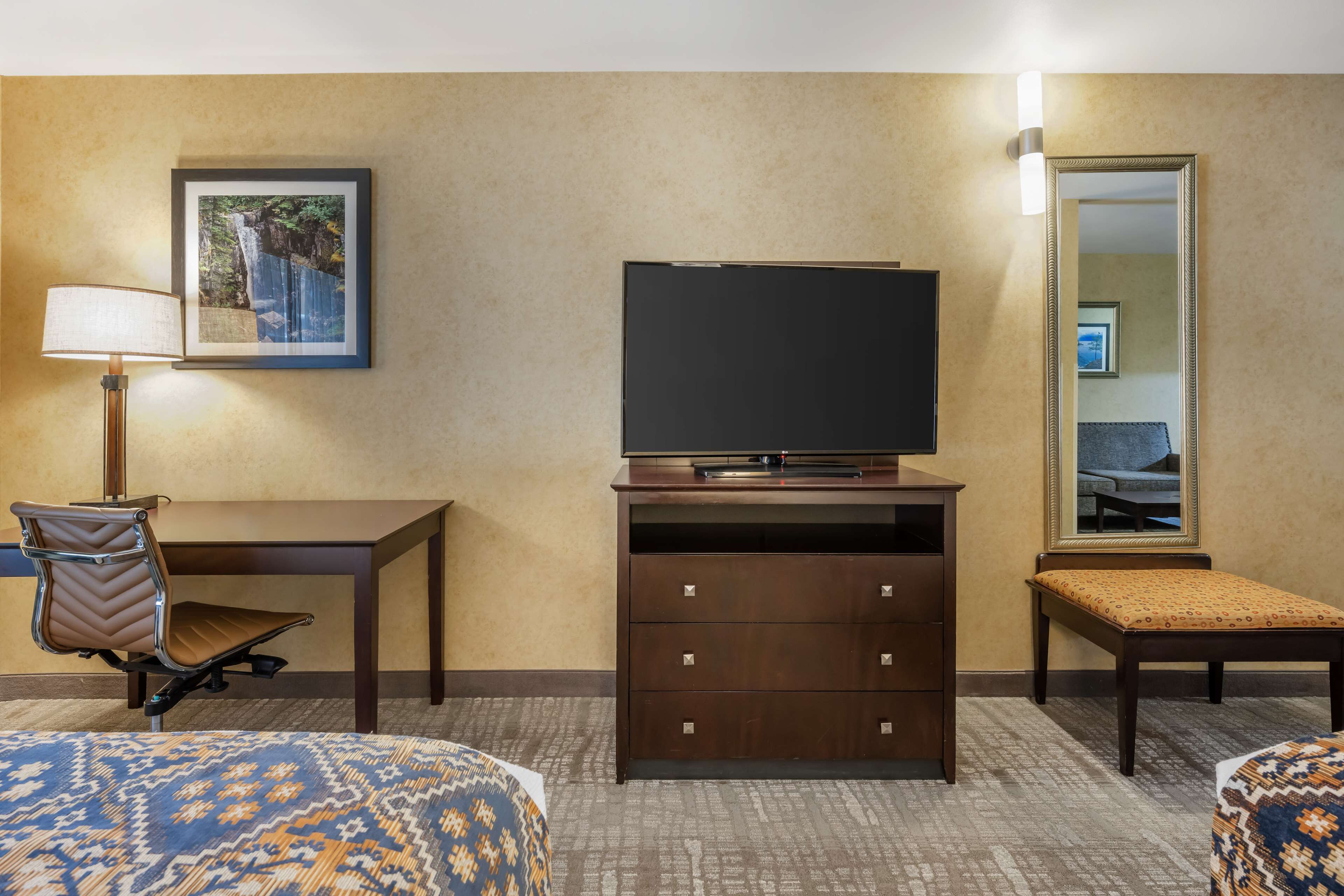 A hotel room with a desk, chair, television, dresser, and a bed.