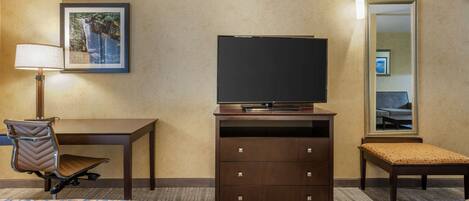 A hotel room with a desk, chair, television, dresser, and a bed.