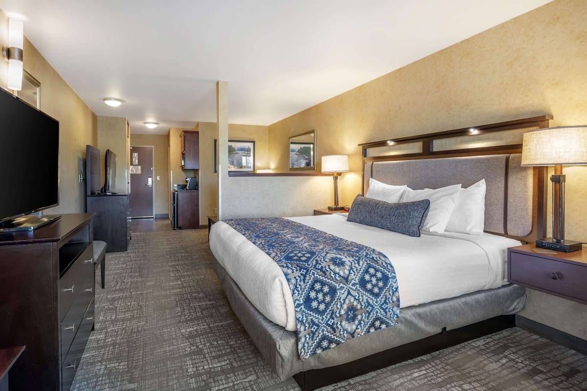 A hotel room with a large bed, a desk, a TV, and a bathroom visible in the background.