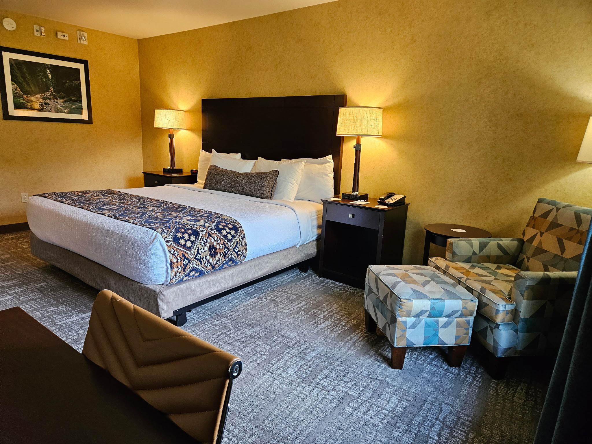 A hotel room with a large bed, two bedside tables, a chair, and a desk with a telephone.