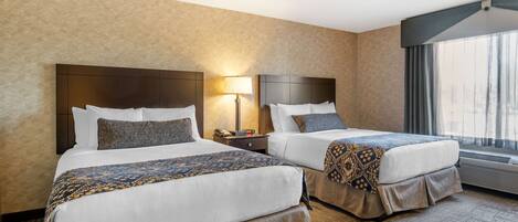 A hotel room with two beds, a nightstand with a lamp, and a large window with curtains.