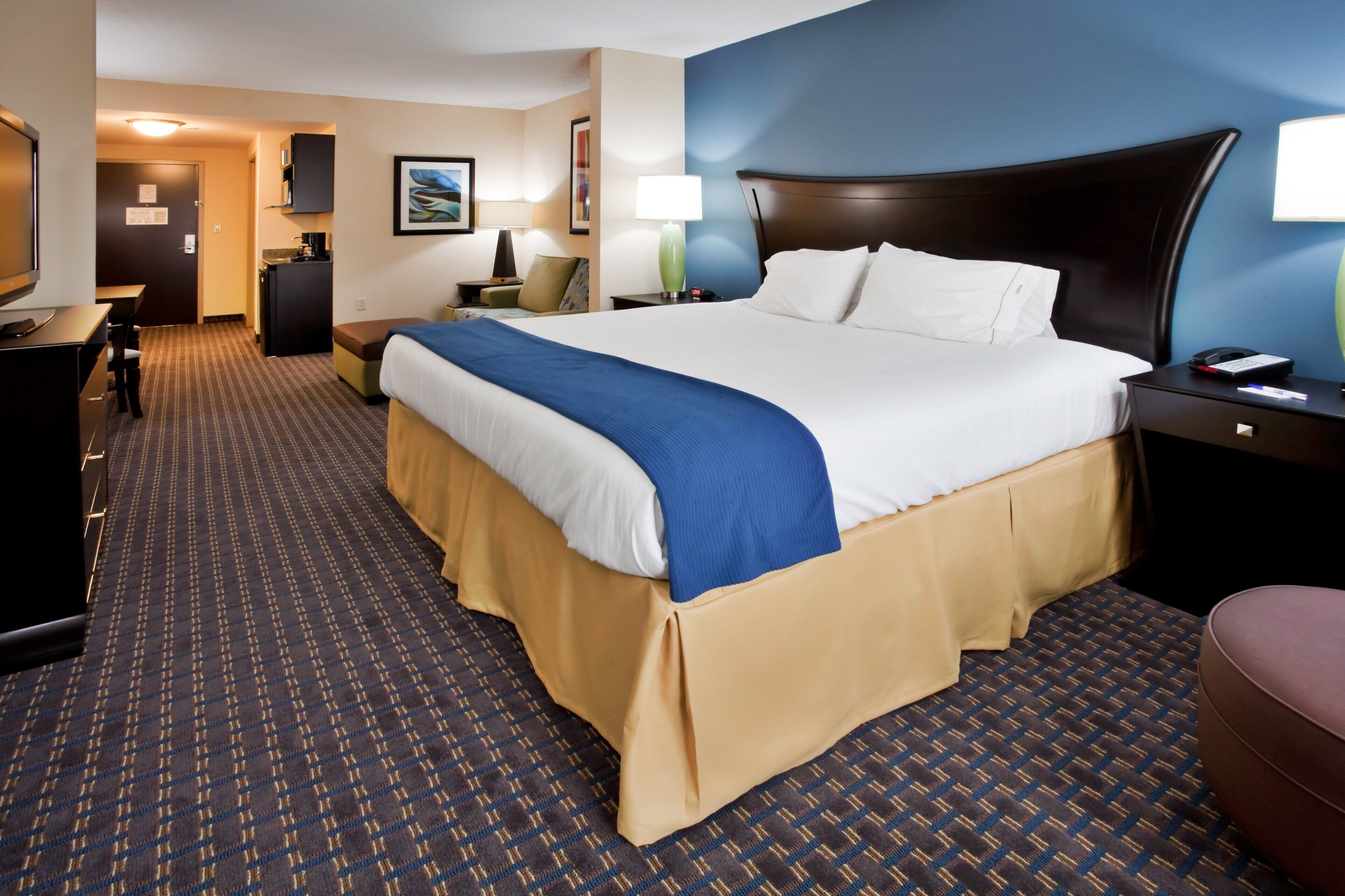 A hotel room with a bed, bedside table, lamp, and a desk with a chair.