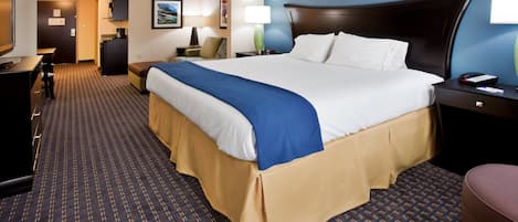 A hotel room with a bed, bedside table, lamp, and a desk with a chair.
