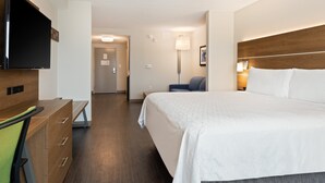 A hotel room with a bed, a desk with a chair, a television, and a lamp.