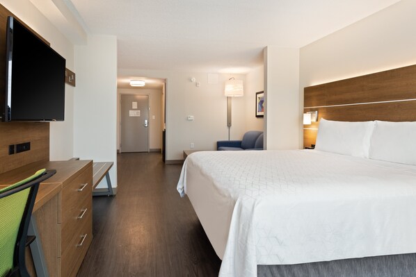 Habitación de hotel con cama, escritorio, silla, televisor y lámpara.