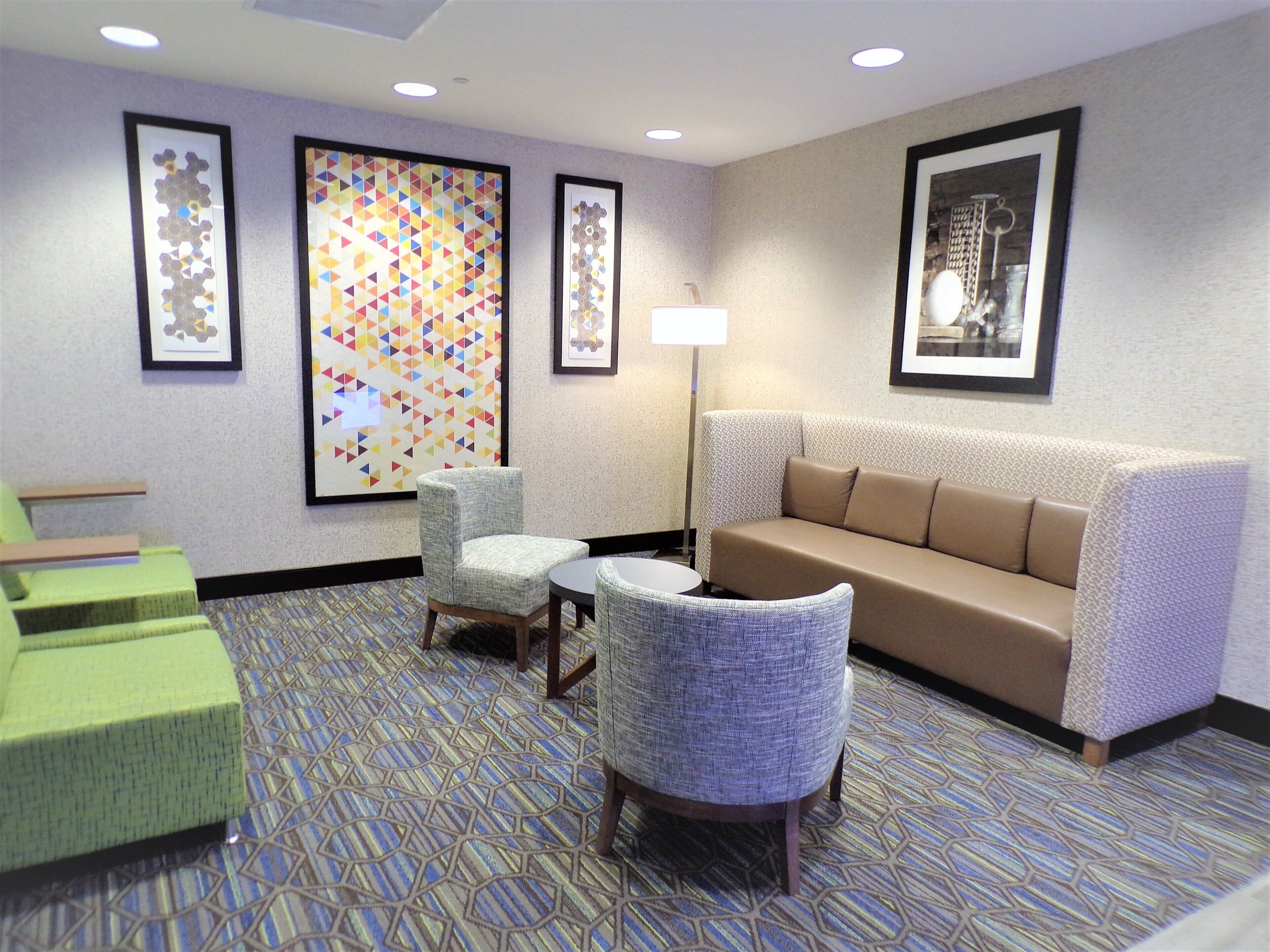 A hotel lobby with a patterned carpet, a sofa, two armchairs, a small table, and framed artwork on the walls.