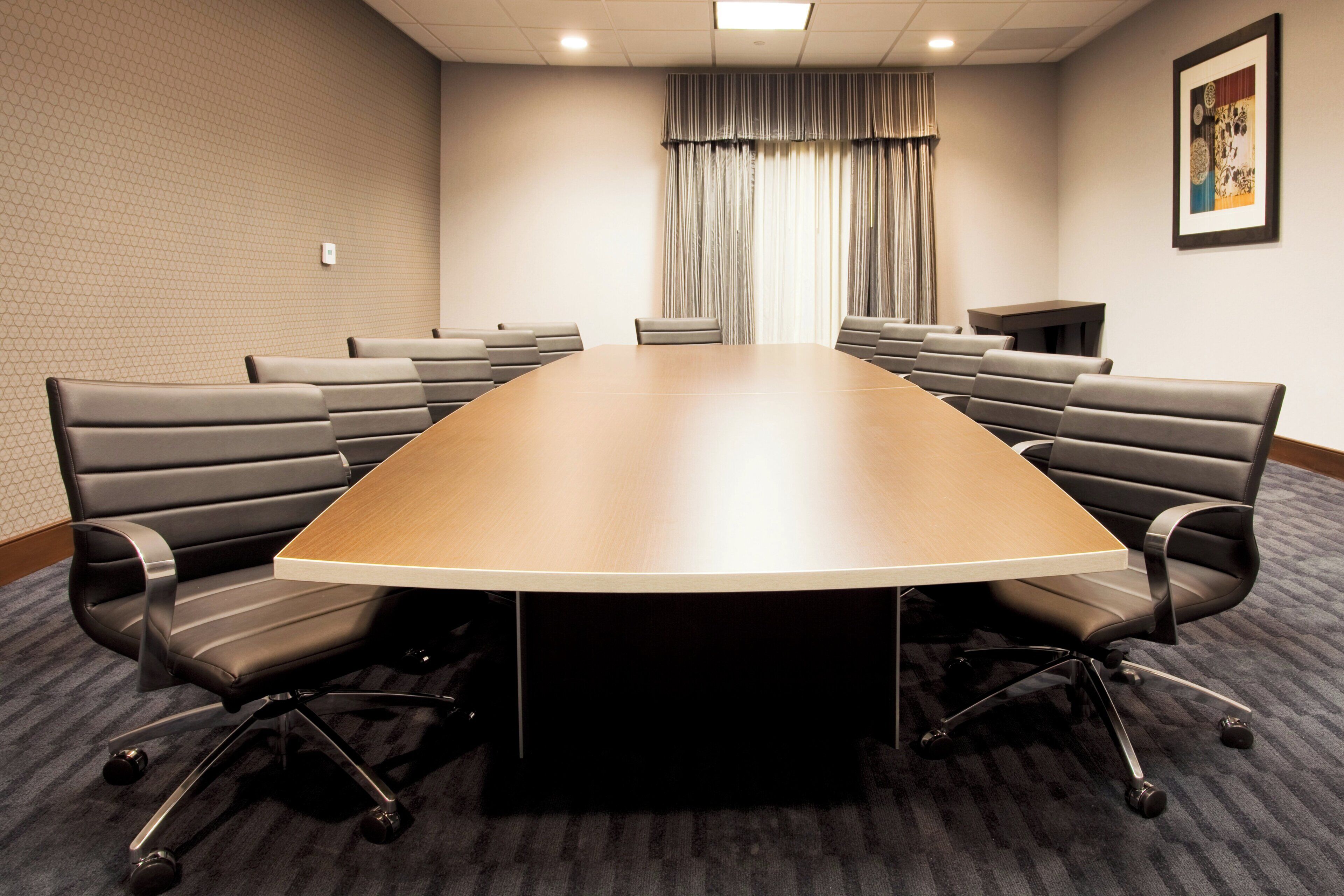 A conference room with a large oval table, multiple chairs, a small table, and a curtain.