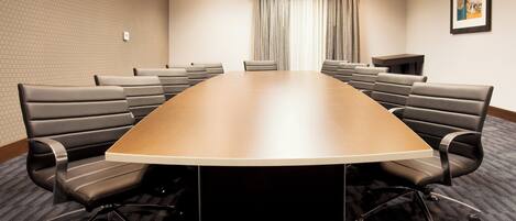 A conference room with a large oval table, multiple chairs, a small table, and a curtain.