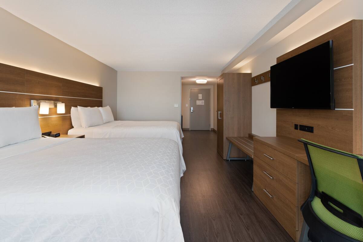 A hotel room with two beds, a desk, a chair, a TV, and a wardrobe.