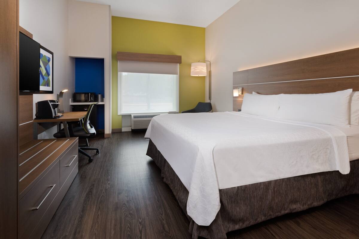 A hotel room with a bed, desk, chair, and a television.