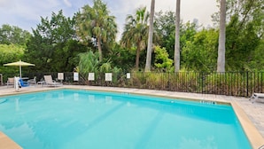 A swimming pool with lounge chairs and umbrellas, surrounded by a fence and trees.