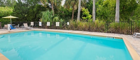Une piscine entourée d’une clôture et d’arbres, avec des chaises longues et des parasols.