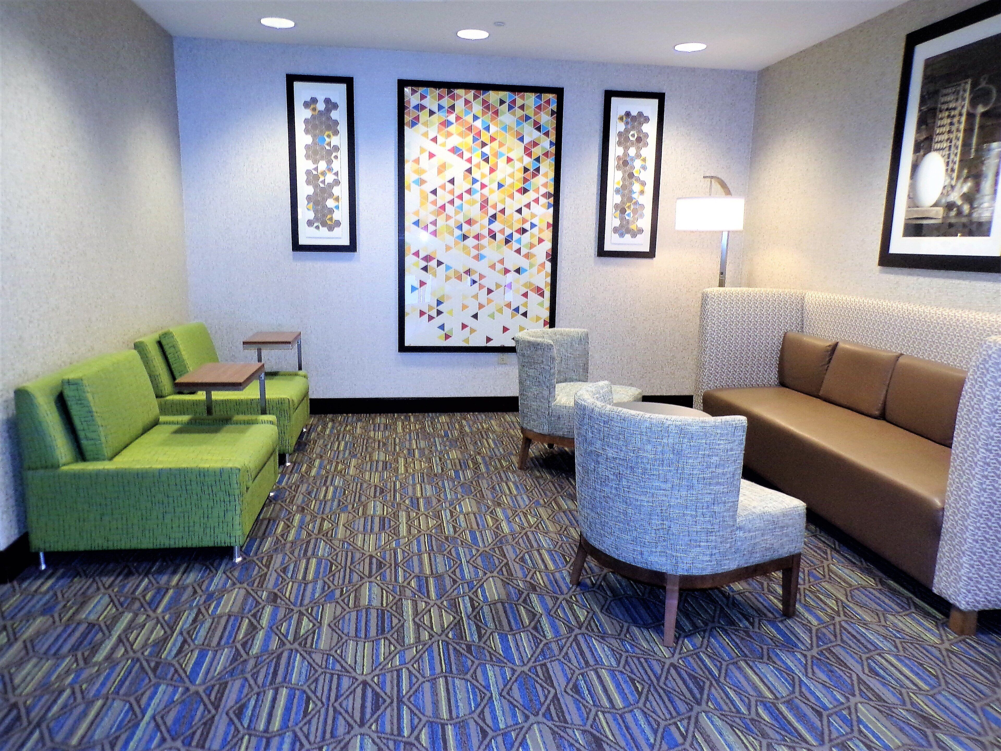 A hotel lobby with a green sofa, a brown sofa, and two armchairs. There are framed artworks on the wall and a patterned carpet.