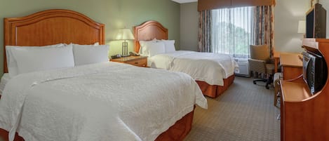 A hotel room with two beds, a desk, a chair, a TV, and a window with curtains.