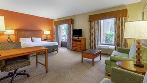 Habitación de hotel con cama, escritorio, sofá, televisor y ventana con cortinas.