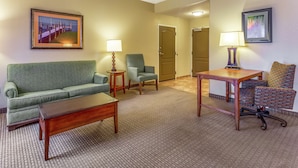 Habitación de hotel con un sofá verde, una mesa de centro de madera, un sillón estampado y dos lámparas.