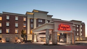 A Hampton Inn & Suites hotel with a brick facade, large entrance, and illuminated signage.