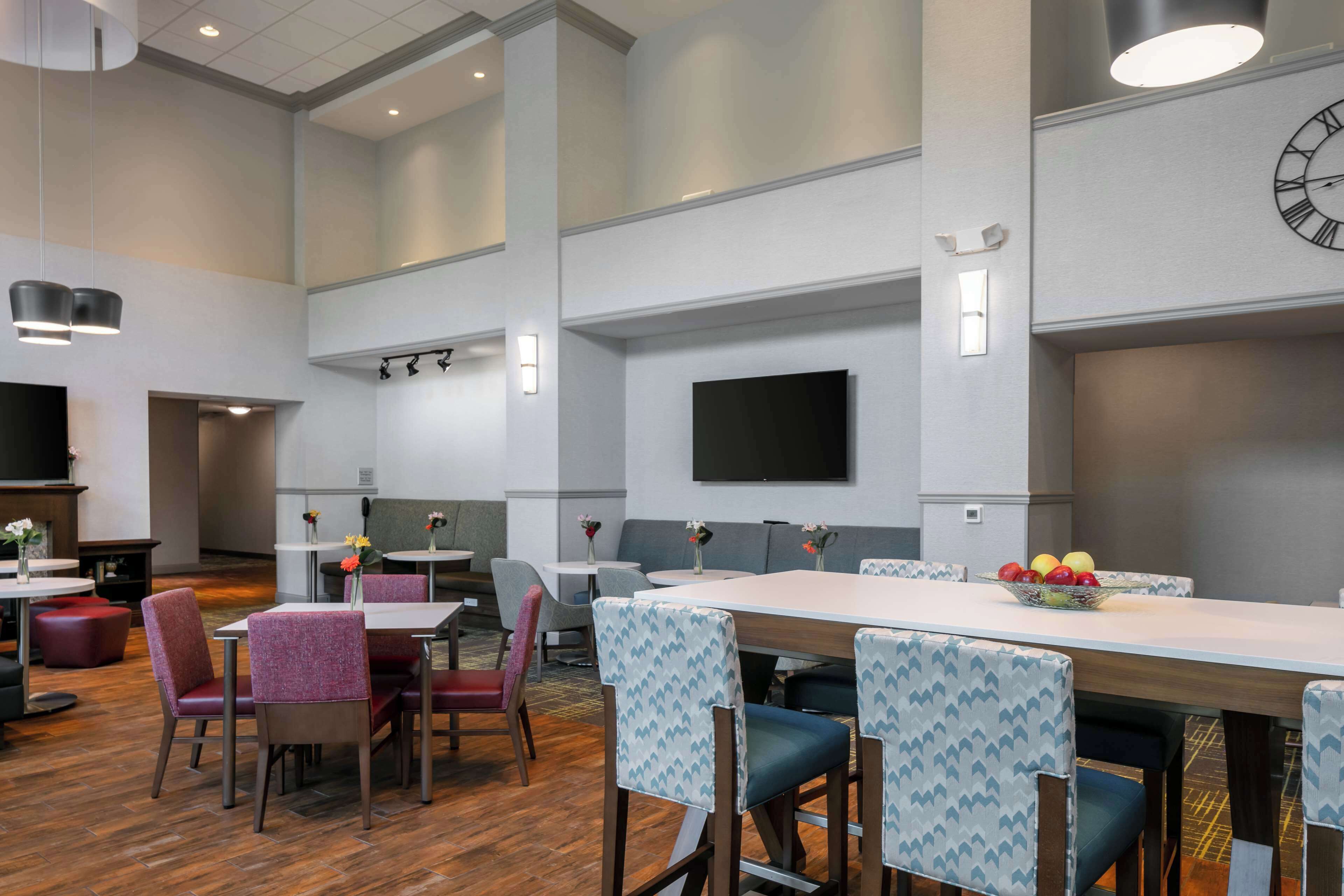 Un espace repas moderne avec une longue table, des chaises rembourrées et un téléviseur à écran plat fixé au mur.