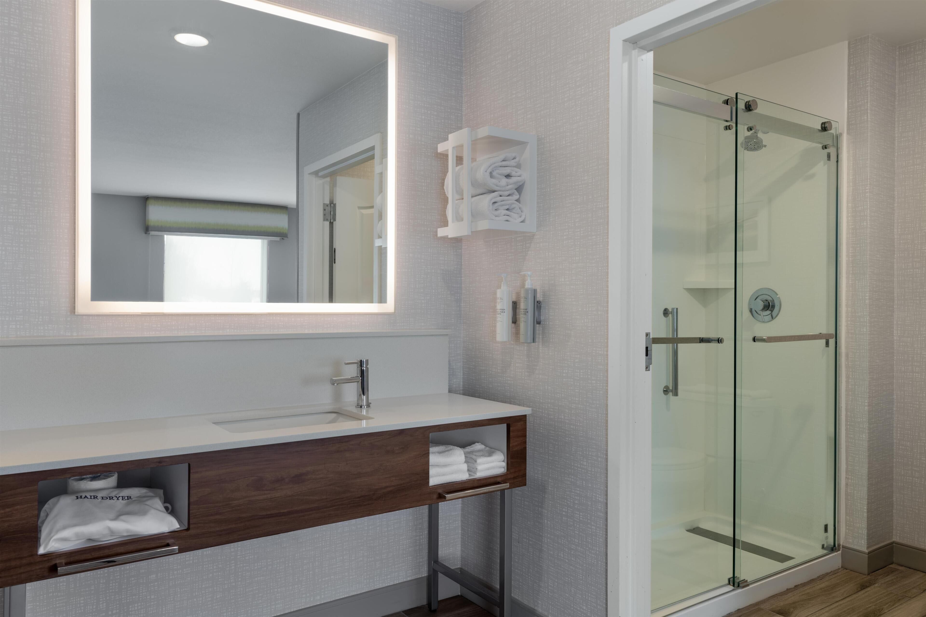 A modern bathroom with a glass shower enclosure, a large mirror, and a wooden vanity with a towel rack.