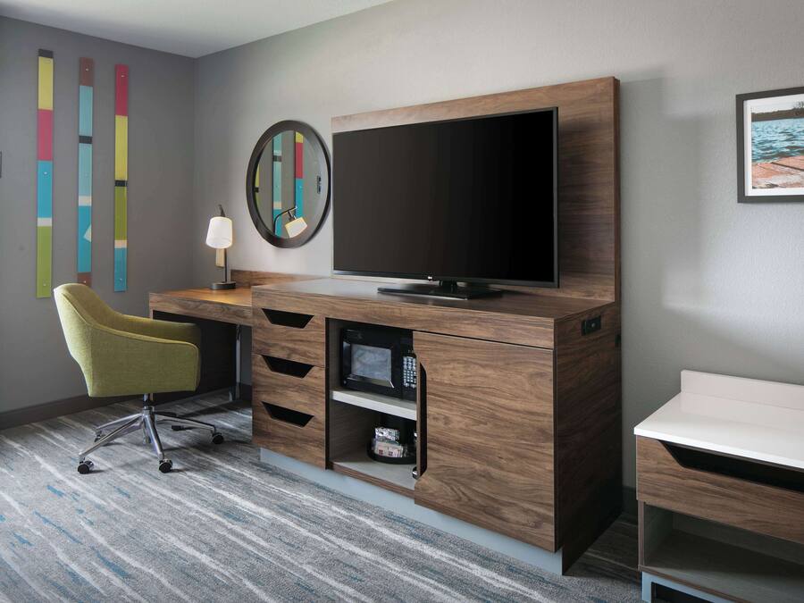 Una habitación de hotel moderna con un escritorio de madera, un televisor de pantalla plana, una silla amarilla, una mesita y una pared decorada con arte colorido.