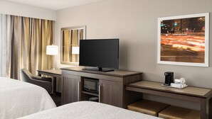 A hotel room with a bed, a desk with a television, a coffee maker, and a framed picture on the wall.
