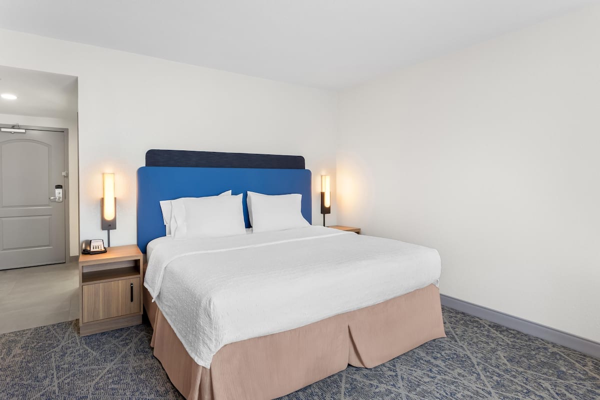 A hotel room with a bed, bedside tables, and a door.