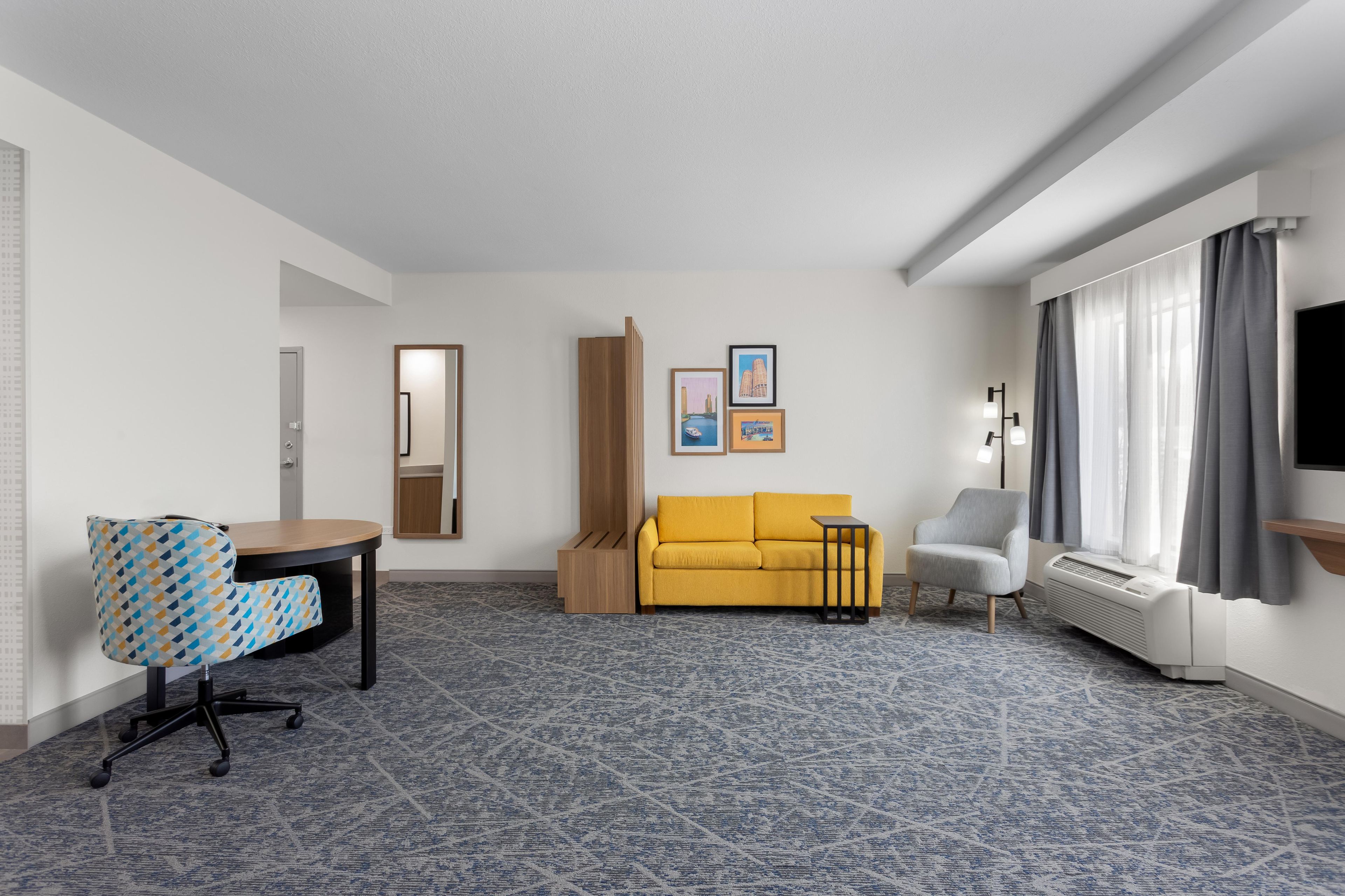 A hotel room with a sofa, a desk, a chair, a small table, a floor lamp, and a television.