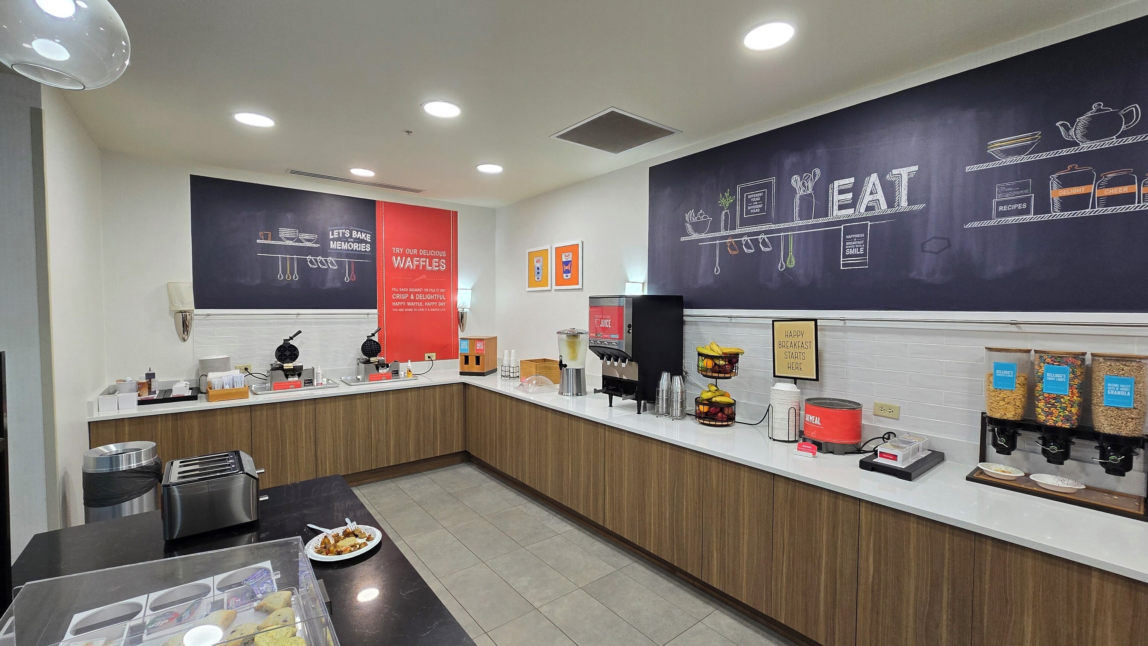 Un espace cuisine moderne équipé d’appareils à gaufres, d’un distributeur de jus et de différents récipients pour aliments.