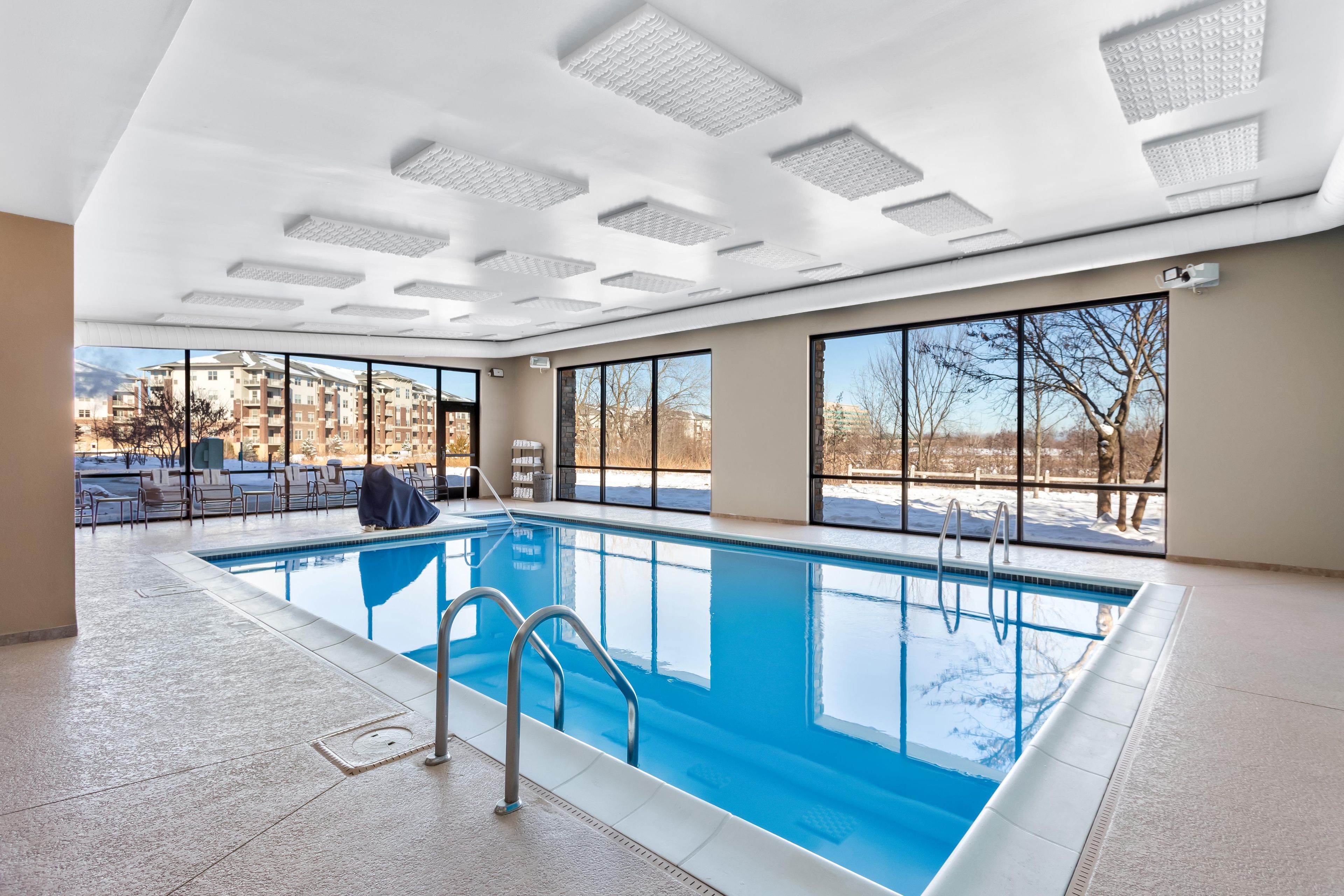 Una piscina interior con paredes de vidrio transparente, suelo de baldosas e iluminación empotrada en el techo.