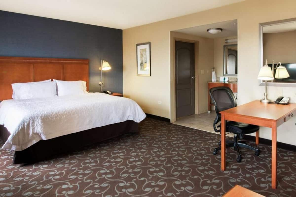 A hotel room with a bed, desk, chair, lamp, and a door leading to a bathroom.