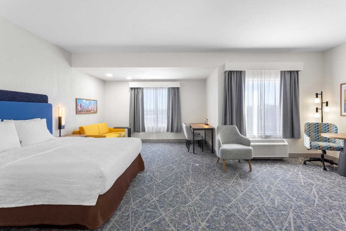 A hotel room with a large bed, a desk, a chair, and a sofa.