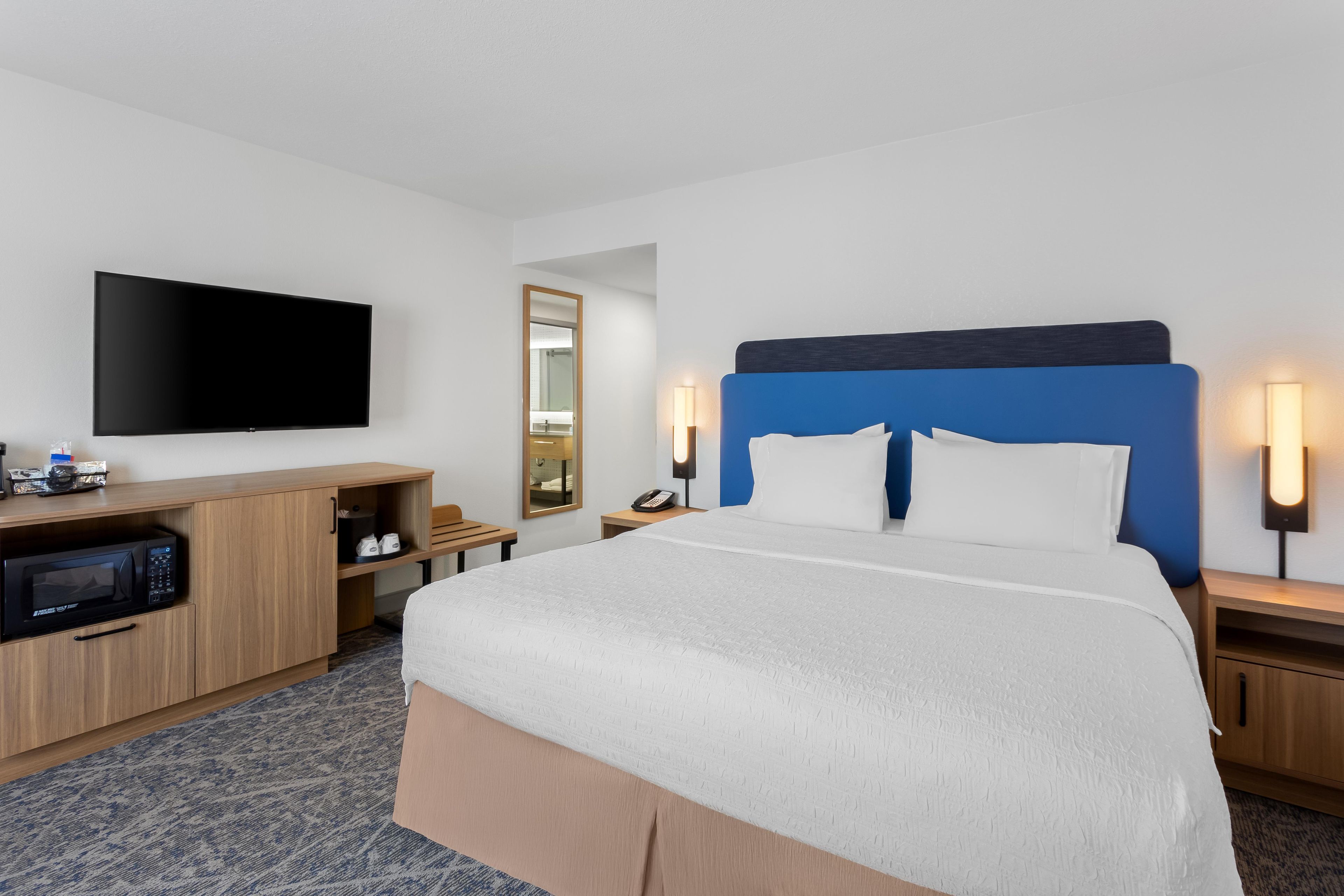 Ein Hotelzimmer mit einem Bett, einem Flachbildfernseher, einer Mikrowelle, einem Holzschrank und einem Nachttisch mit Telefon.