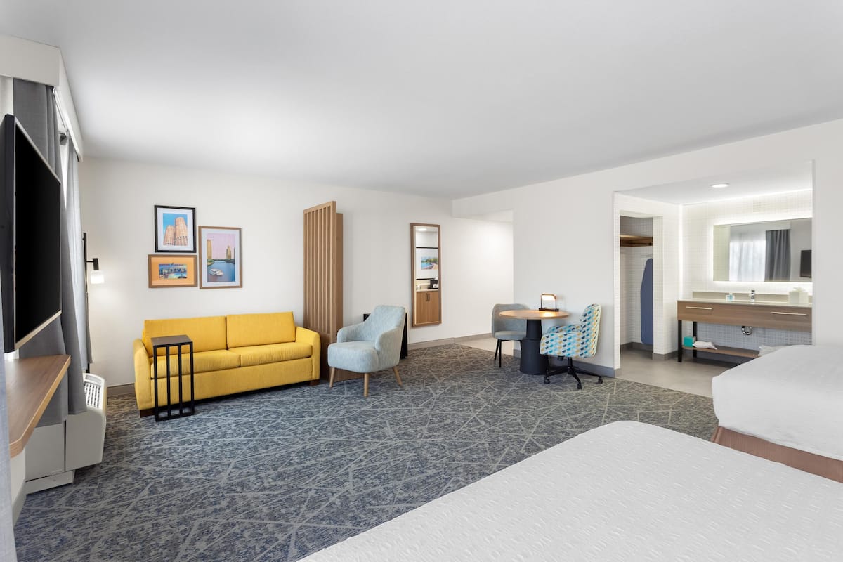 A hotel room with a bed, a sofa, a desk, a chair, a small table, a mirror, and a wardrobe.