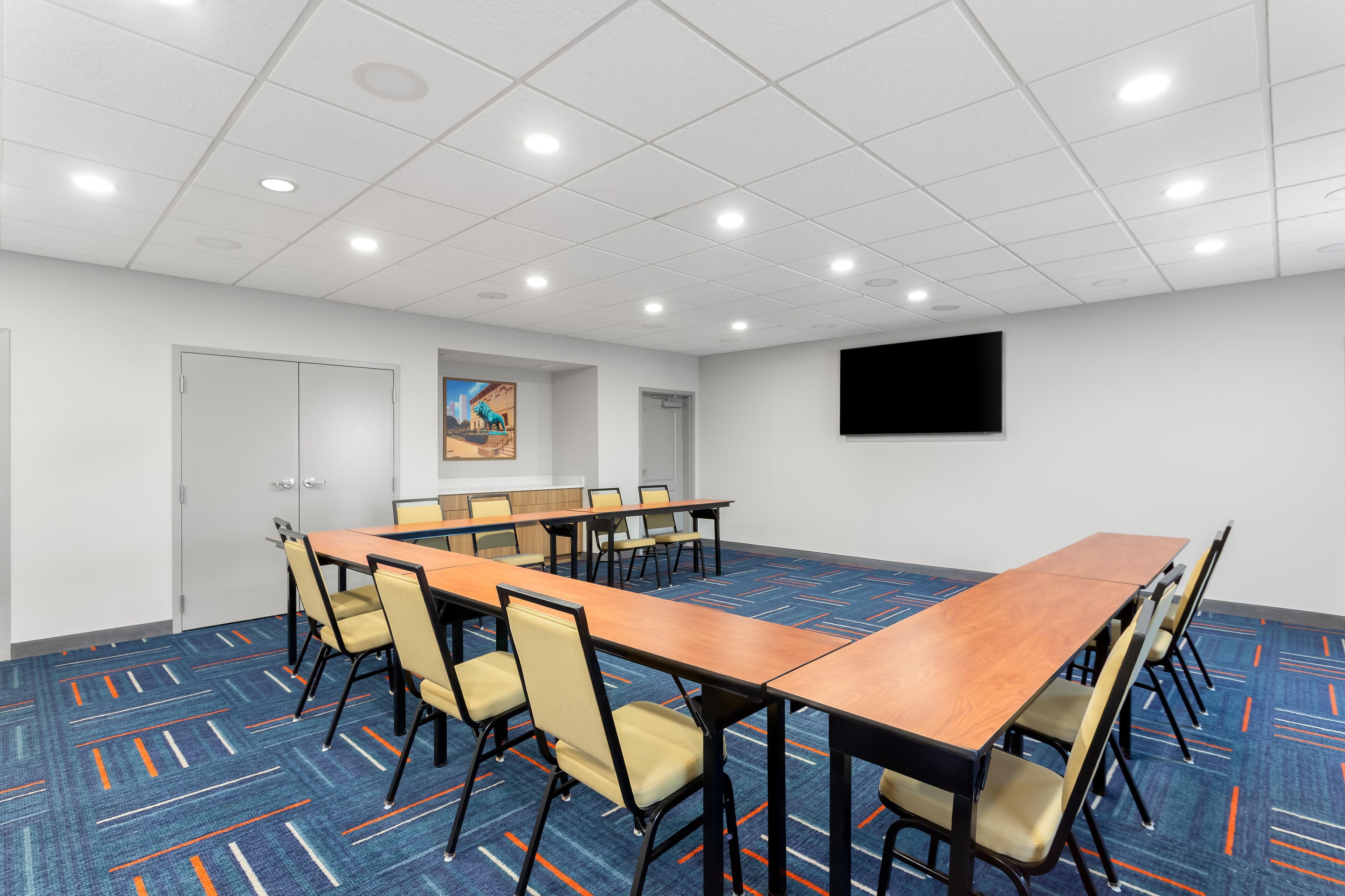 Un salón de conferencias con una mesa larga, sillas, un televisor de pantalla plana y una puerta.