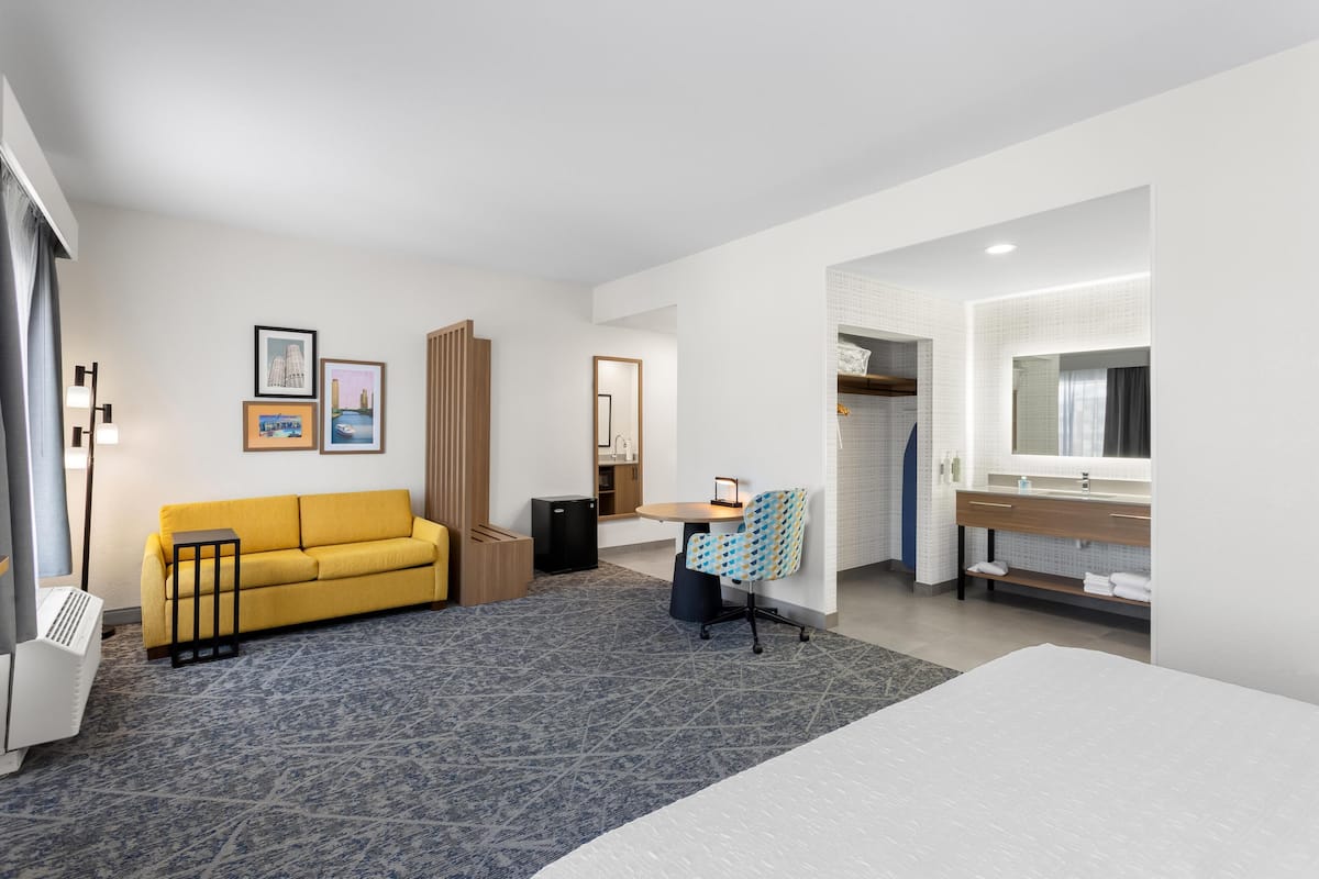 A hotel room with a bed, a sofa, a desk, a chair, a mirror, a wardrobe, and a bathroom.