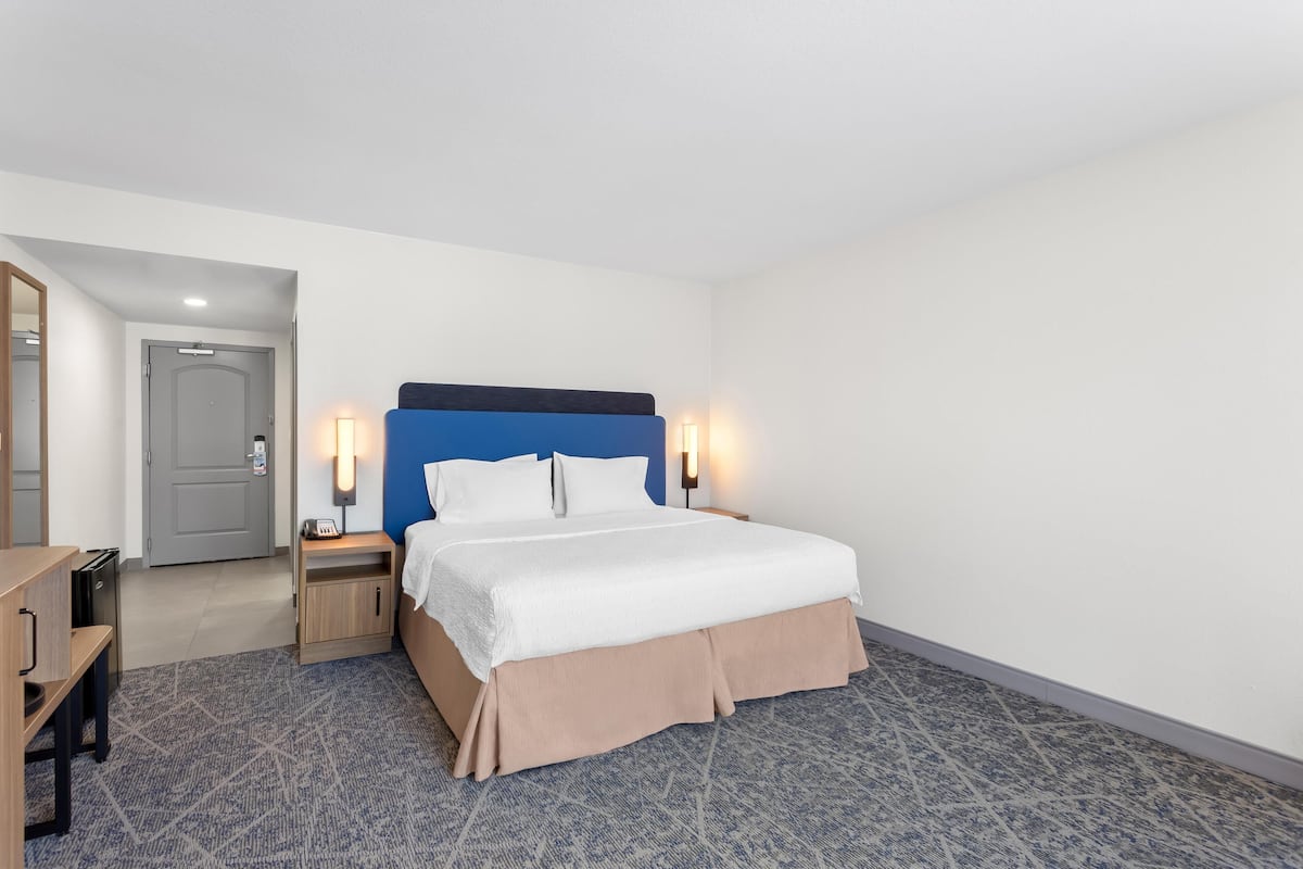 A hotel room with a bed, bedside tables, a desk, and a mirror.