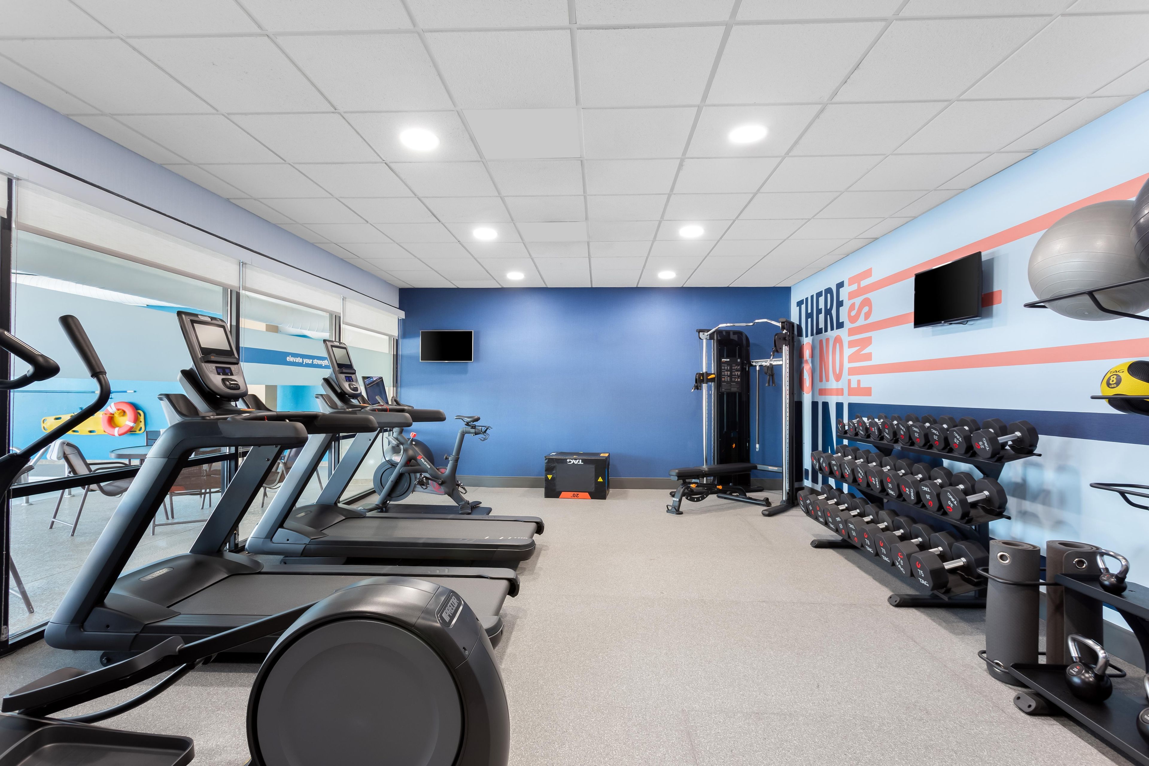 A gym with treadmills, a stationary bike, a weight bench, and a wall with motivational text.