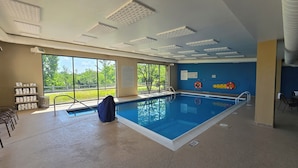 An indoor swimming pool with clear pool rules and no lifeguard signs, surrounded by windows offering a view of greenery.