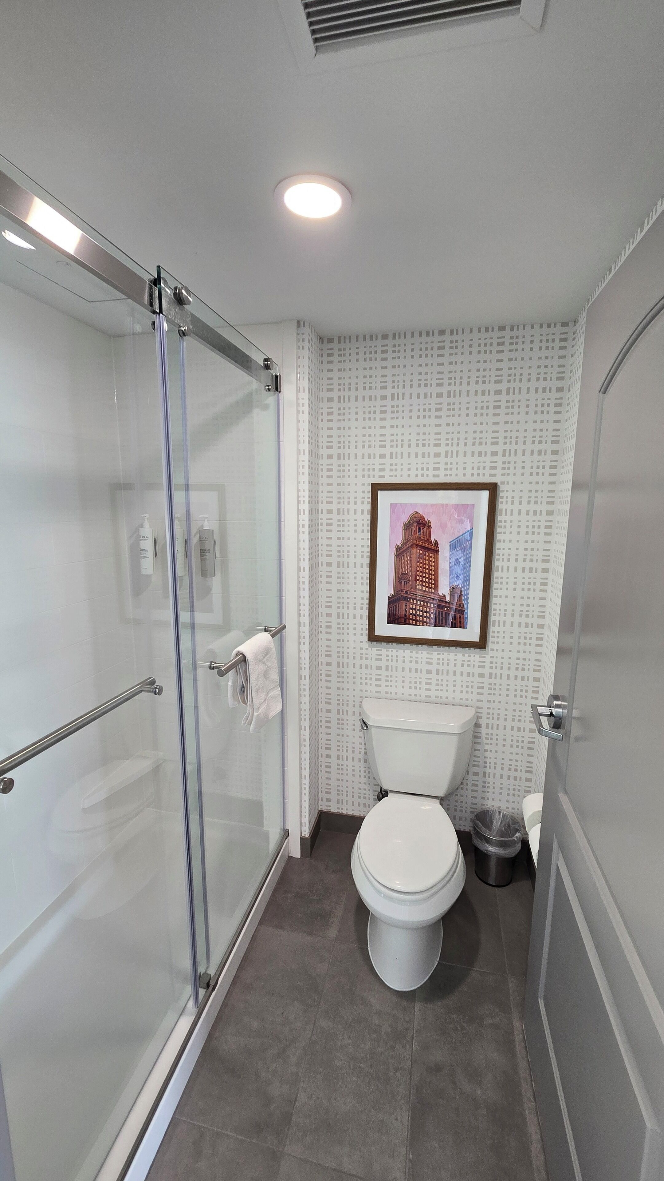 Um banheiro moderno com box de vidro, vaso sanitário e um quadro na parede.
