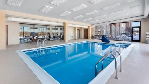 A modern indoor swimming pool with clear glass walls, a poolside seating area, and a view of the outside. - Hampton Inn & Suites Chicago Deer Park (Barrington)