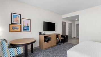 Quarto de hotel com cama, escrivaninha com computador, cadeira, televisão e quadros nas paredes.