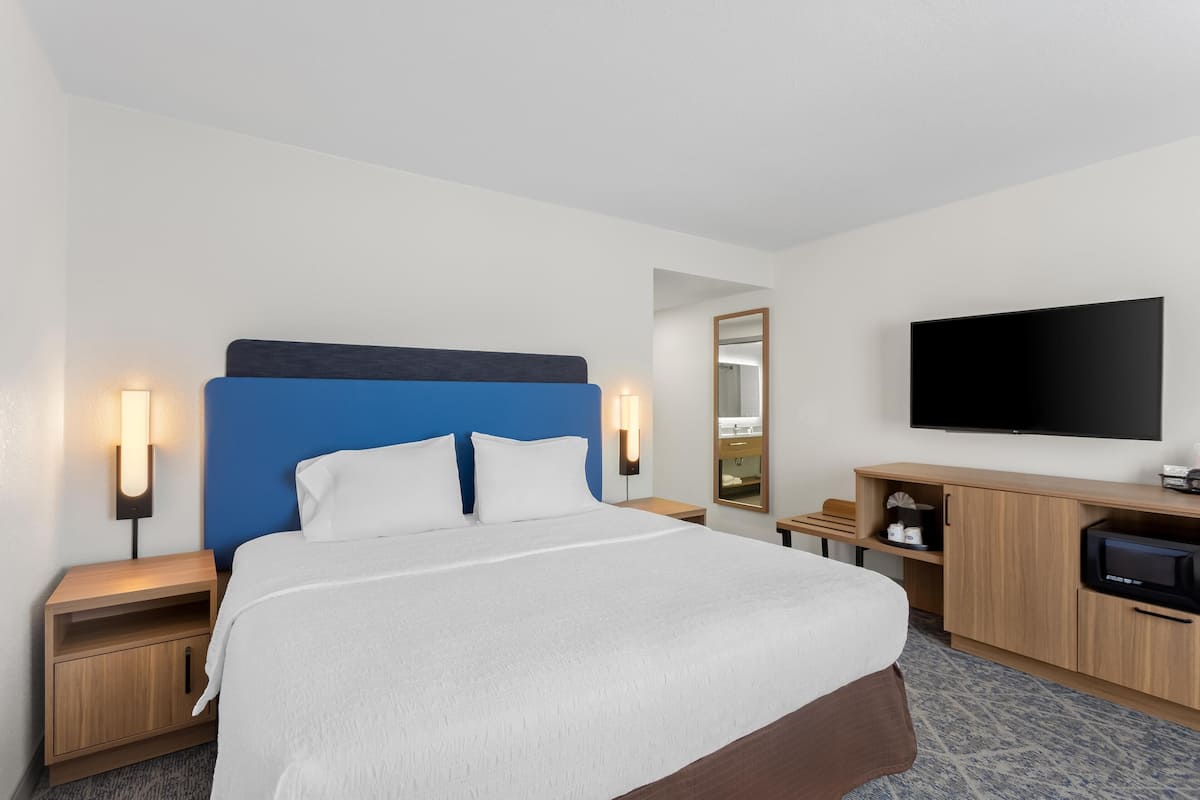 A hotel room with a bed, bedside tables, a TV, a mirror, and a wooden cabinet.