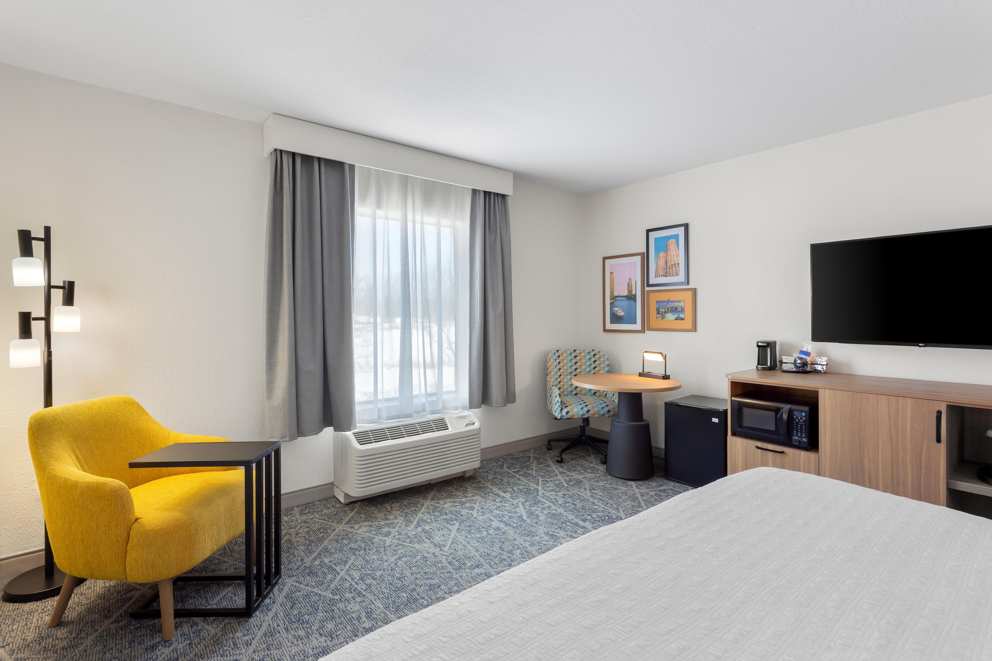 A hotel room with a bed, a desk, a chair, a television, and a window with curtains.