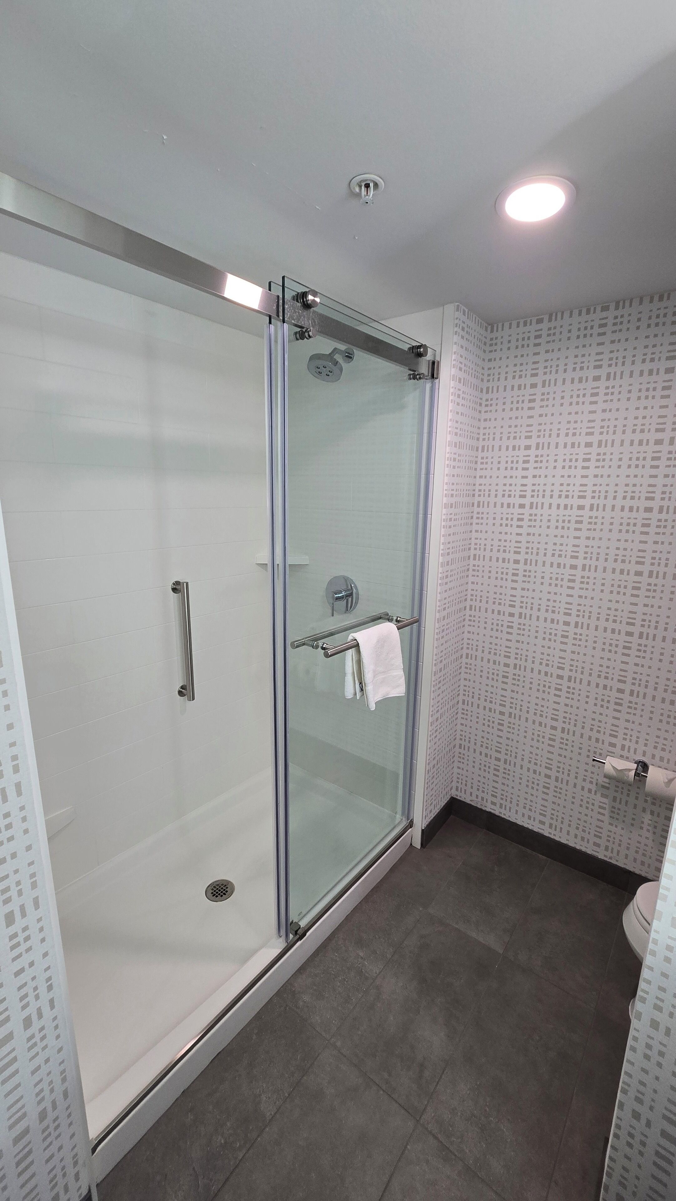 A modern bathroom with a glass-enclosed shower, a towel rack, and patterned wall tiles.