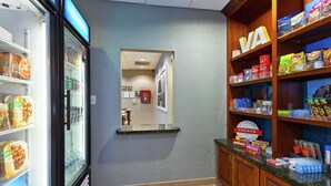 Una despensa de hotel con estantes llenos de refrigerios y bebidas, un refrigerador y un espejo que refleja el interior.