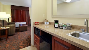 Una habitación de hotel con kitchenette, un sofá, una mesa de comedor y un espejo grande.