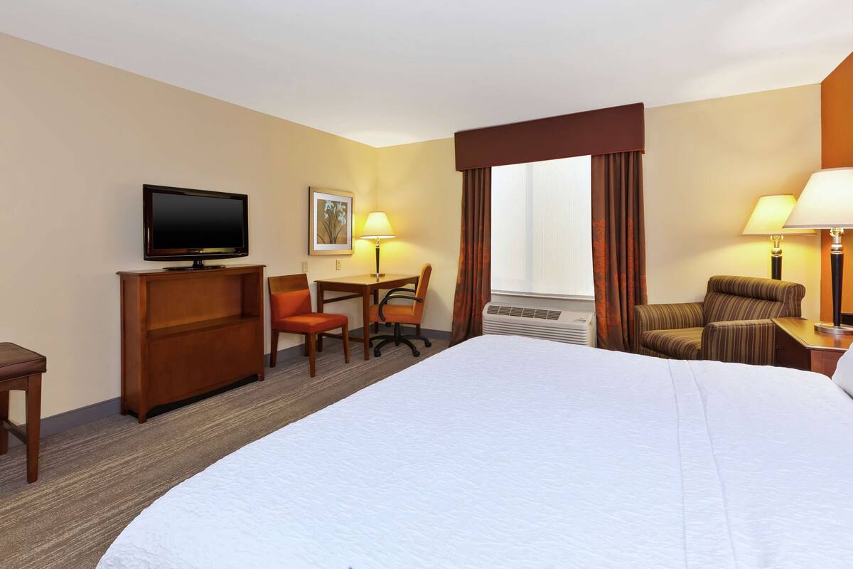 A hotel room with a large bed, a desk with a chair, a television, and two lamps.